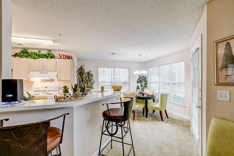 the living room and dining room of an apartment with a kitchen and table and chairs